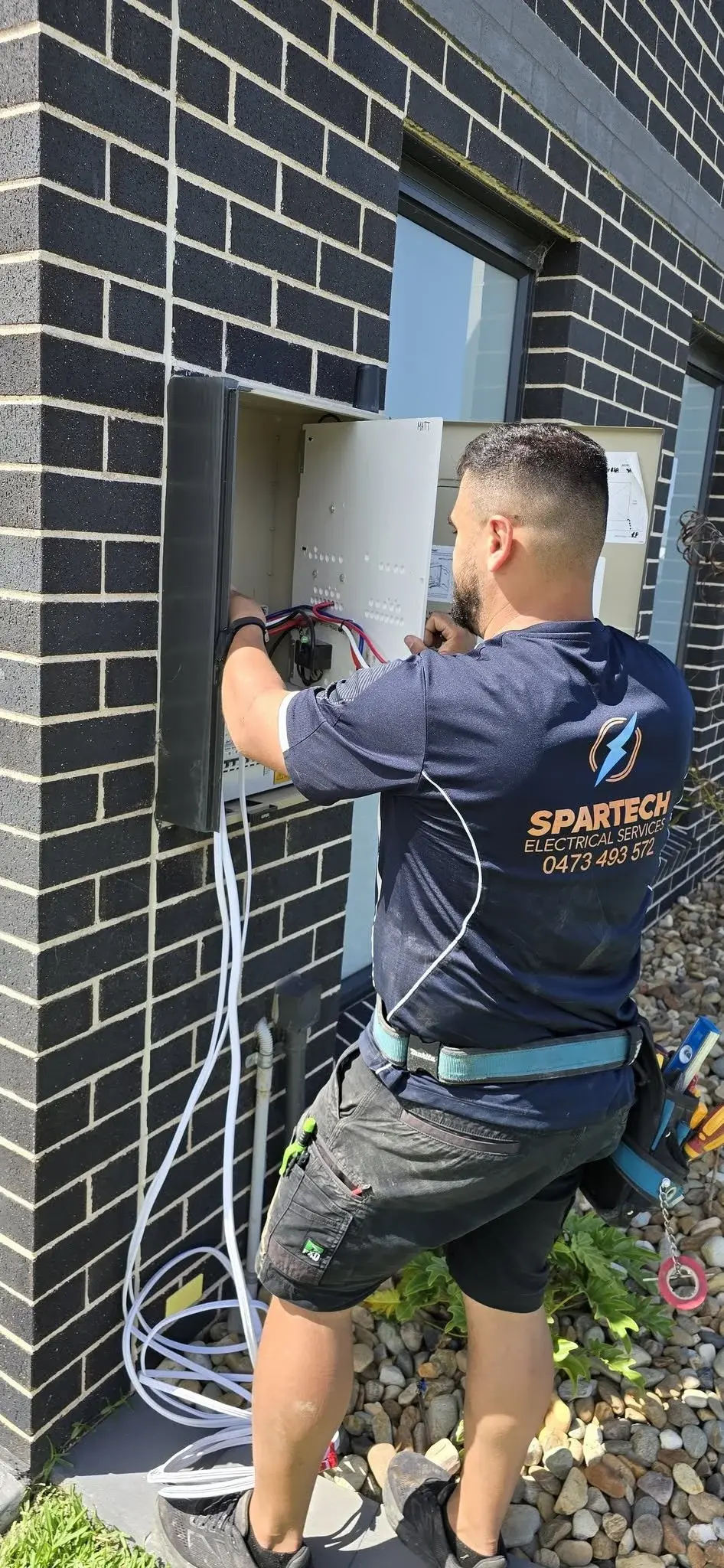 A technician working on an outdoor electrical panel, wearing protective gear.