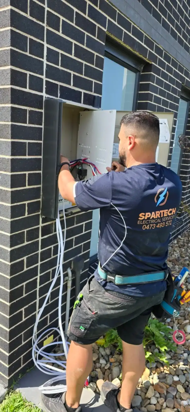 A technician working on an outdoor electrical panel, wearing protective gear.
